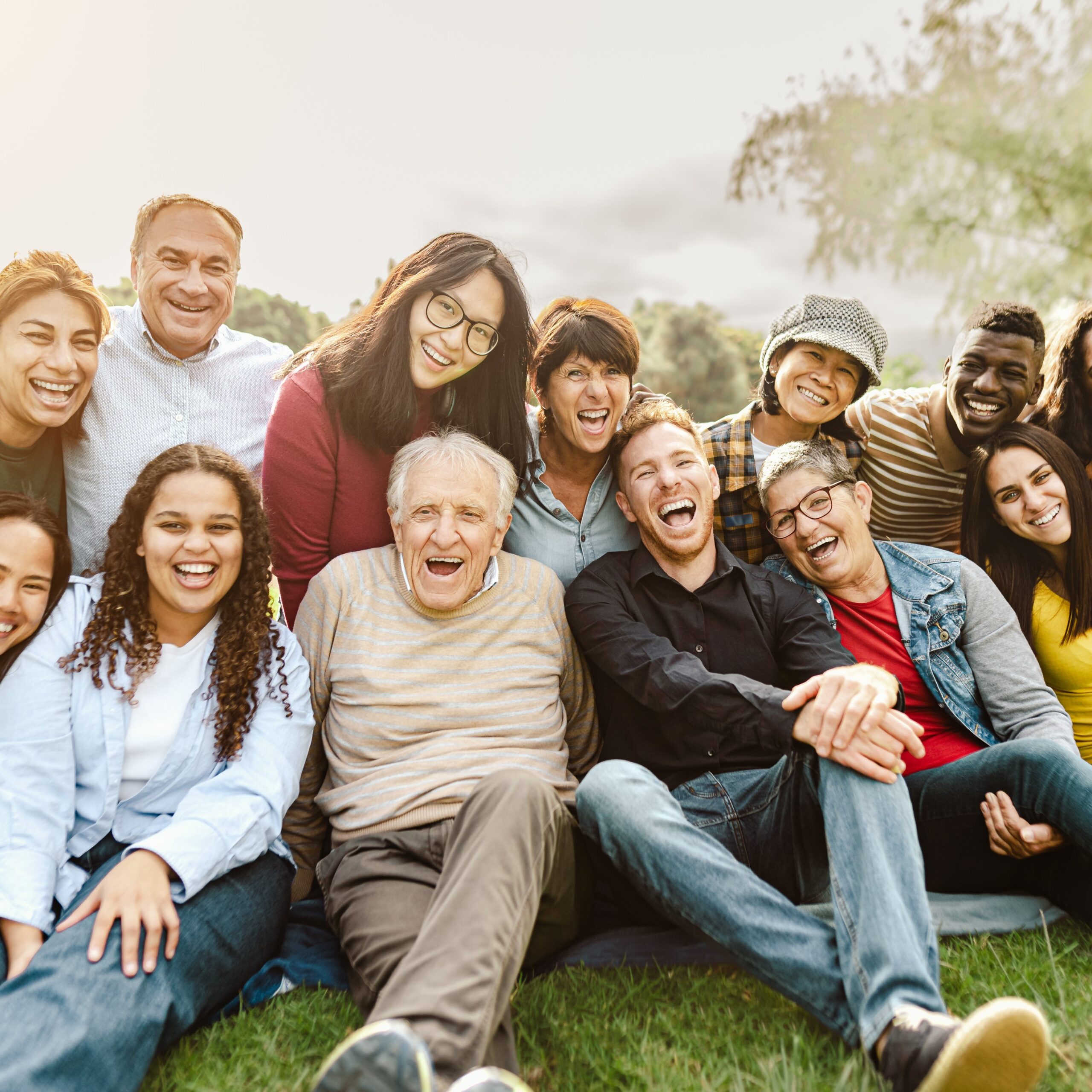 Happy multigenerational people having fun sitting on grass in a public park